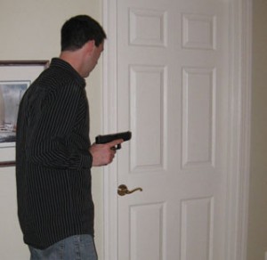 Standing to the left of the door, with the gun close to his body, the author prepares to push open the door and quickly take a step back to his original position.