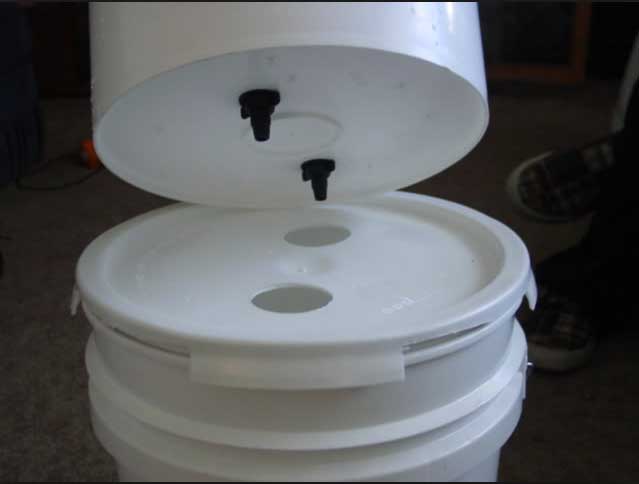The top bucket sits on the lid of the bottom bucket and the filtered water drains down via gravity.